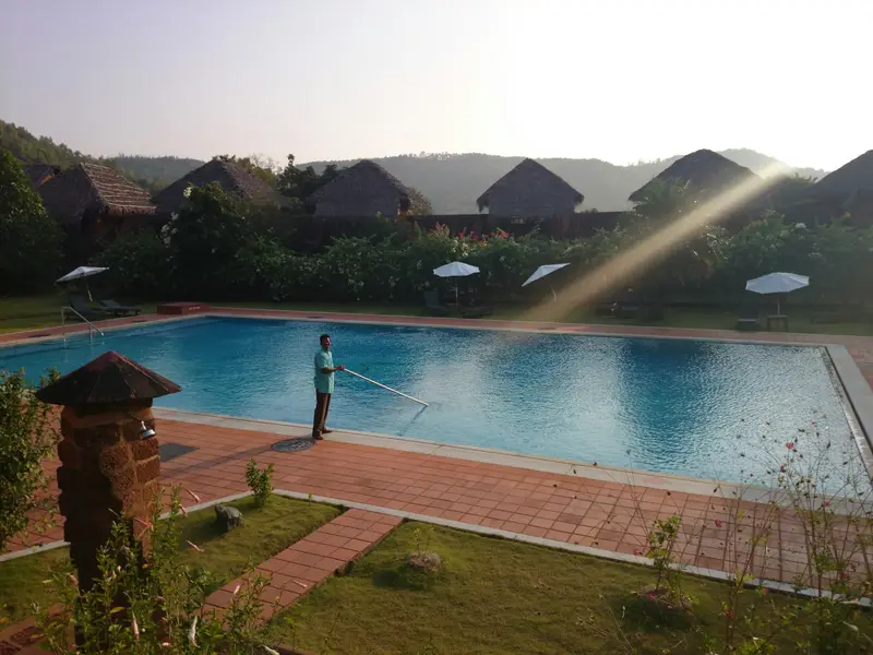 Worker cleaning a pool with a long pole at sunrise