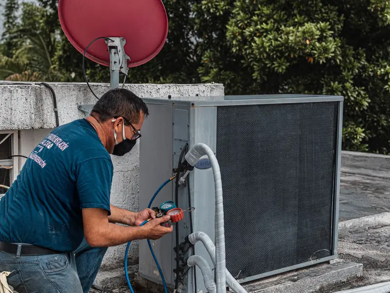 Technician connecting a manifold gauge to an outdoor air conditioner