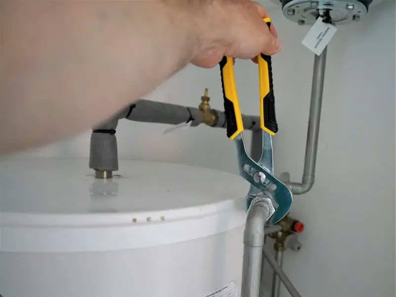Pliers tightening a fitting on top of a tank water heater